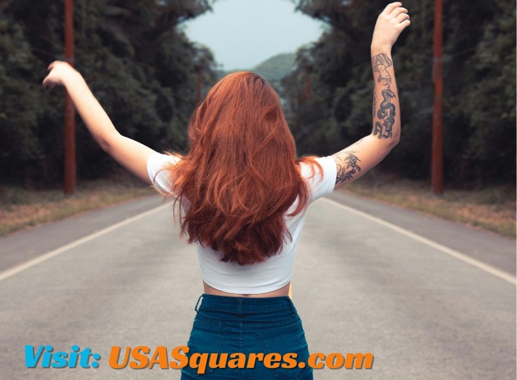 Woman with long red hair and tattooed arms celebrating freedom on an open road - the://vital-mag.net blog