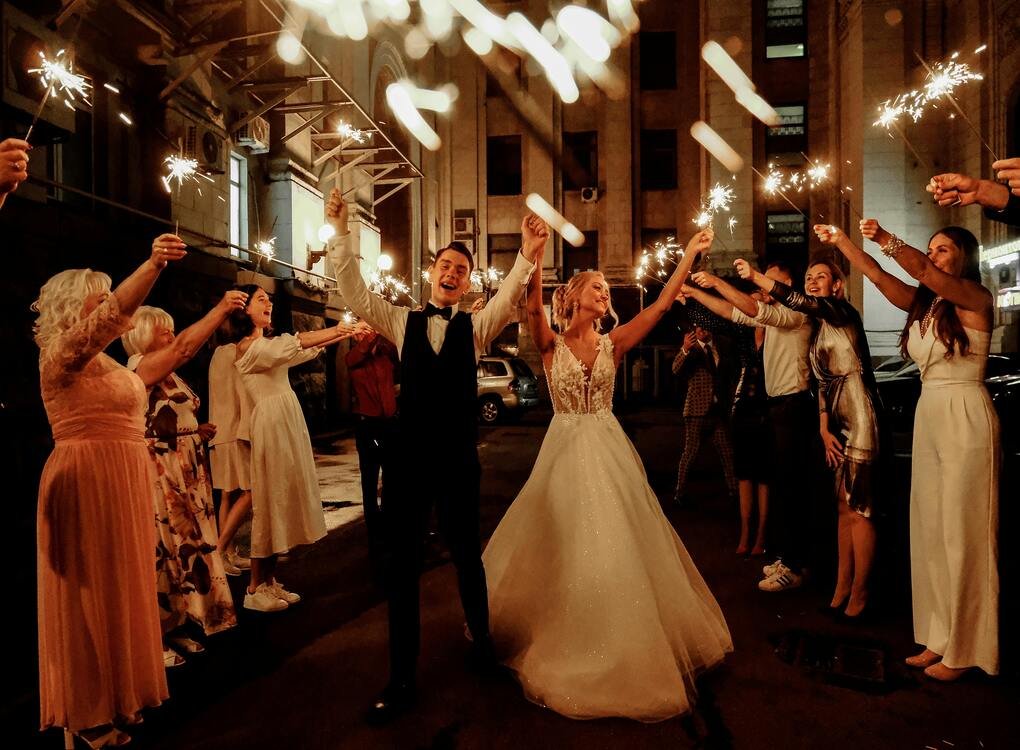 Bride and groom celebrating with sparklers surrounded by guests, symbolizing joy, unity, and memorable moments in relationships.