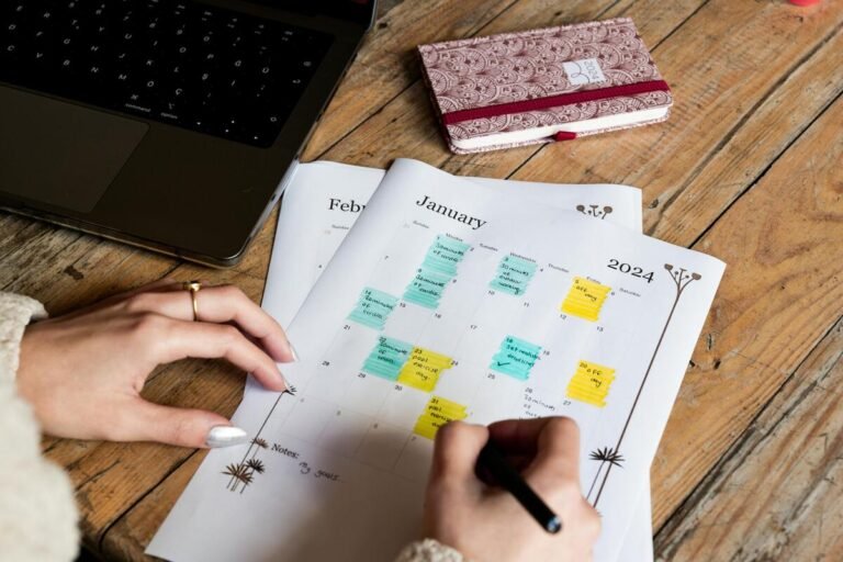 A person planning on Aurora Labor Day Events 2024 calendar with colorful highlights, next to a laptop and a patterned notebook on a wooden table