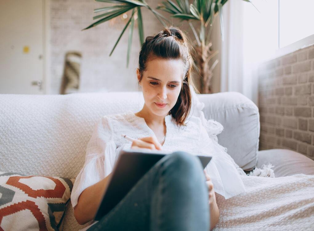 Young woman using a tablet for writing while relaxing on a cozy sofa - http:// tabletwritings.com Blog